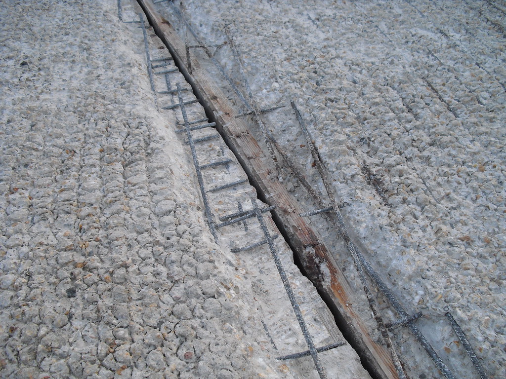 An open diagonal bridge joint, with exposed metal and reinforcing bars between rough concrete surfaces.