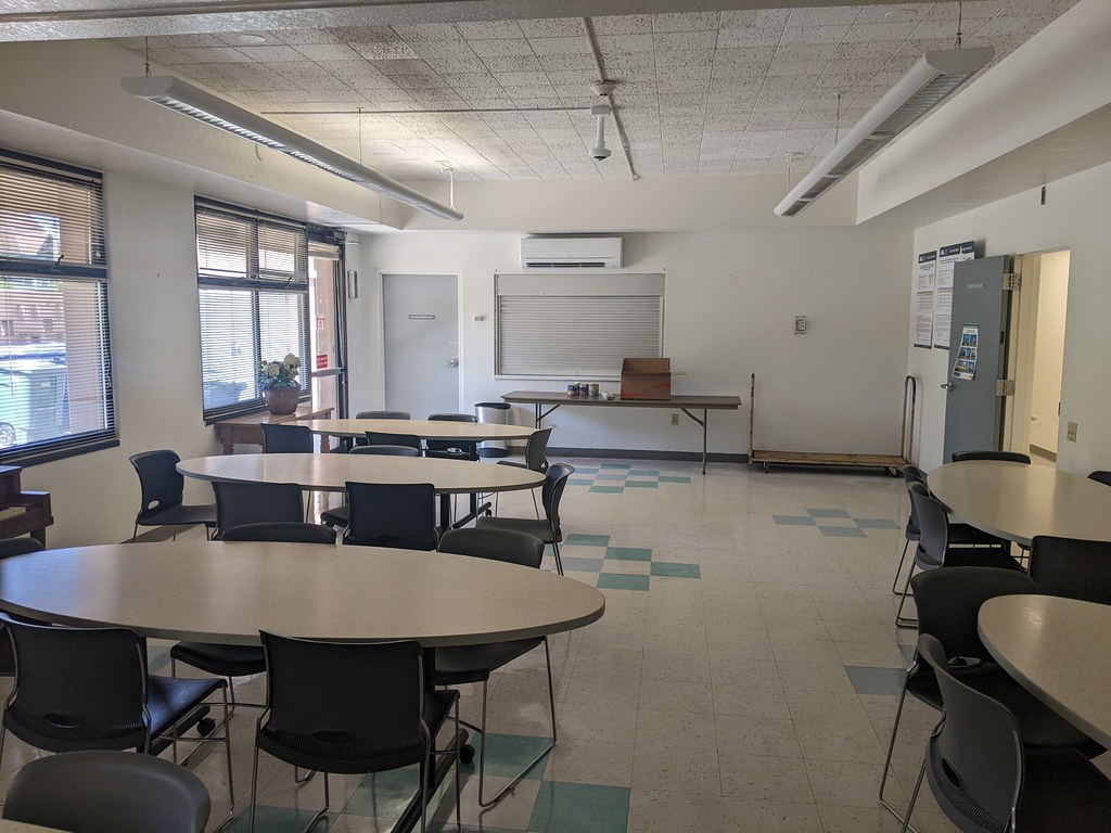 An empty community room with tables, chairs and a wall-mounted air conditioner.