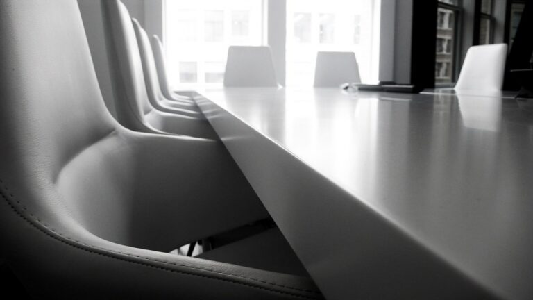 An empty conference table surrounded by black office chairs