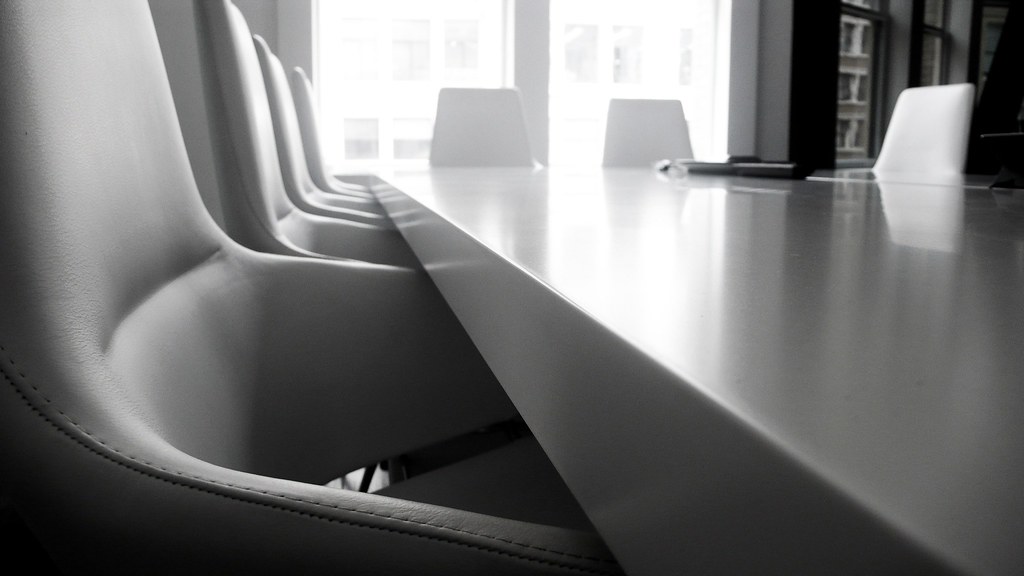 An empty conference table surrounded by black office chairs
