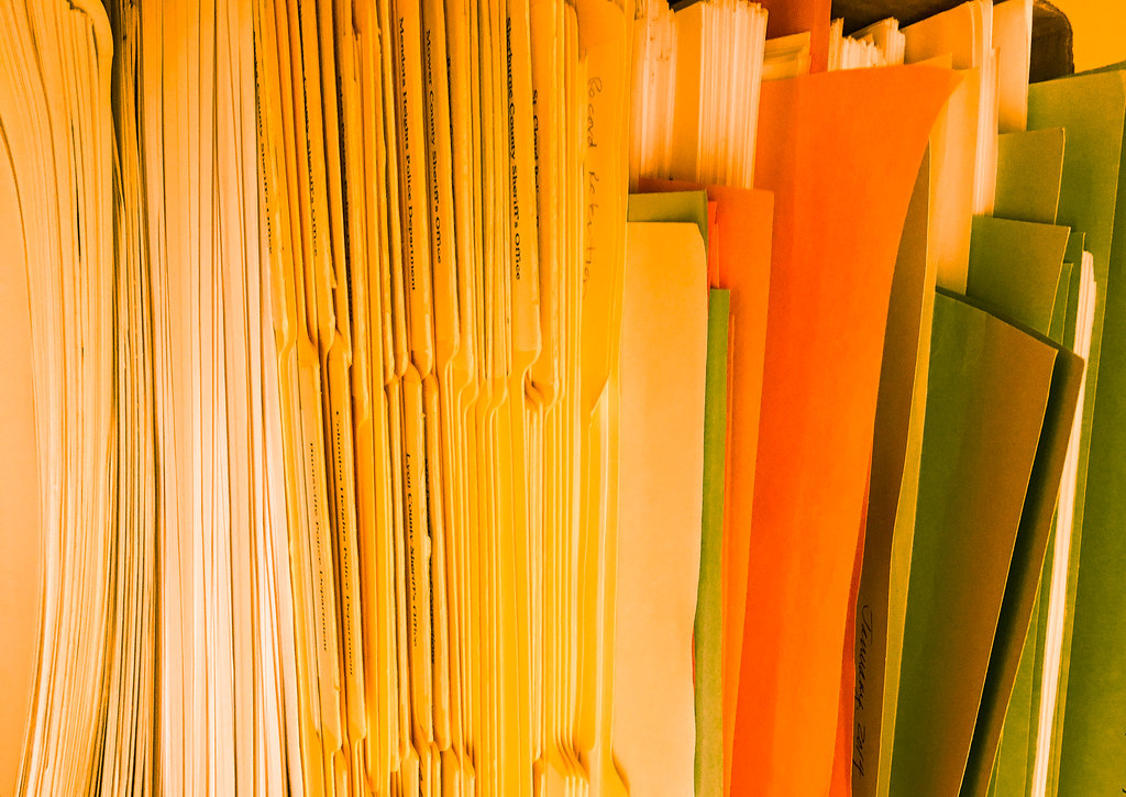 Closely packed paper folders and documents, with cream, orange and green covers.