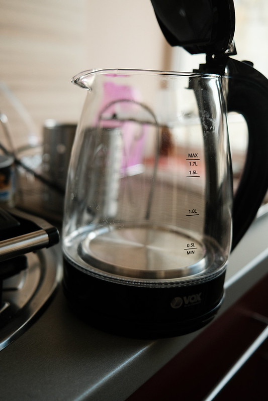 A transparent glass electric kettle filled with water on a kitchen counter beside wooden utensils