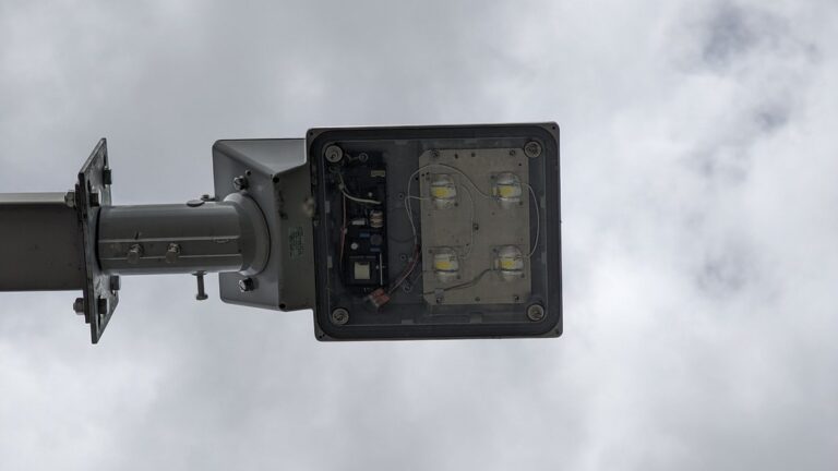 Underside of a rectangular LED street-light fitting mounted on a metal arm against a cloudy sky.