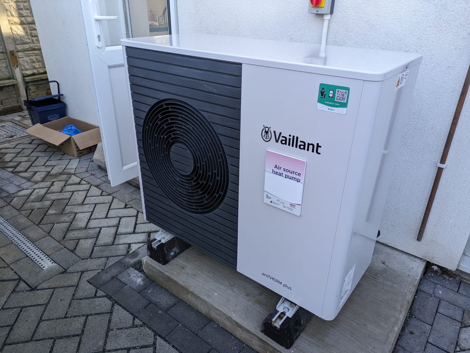 Outdoor air-source heat pump installed beside the rendered wall of a terraced house.