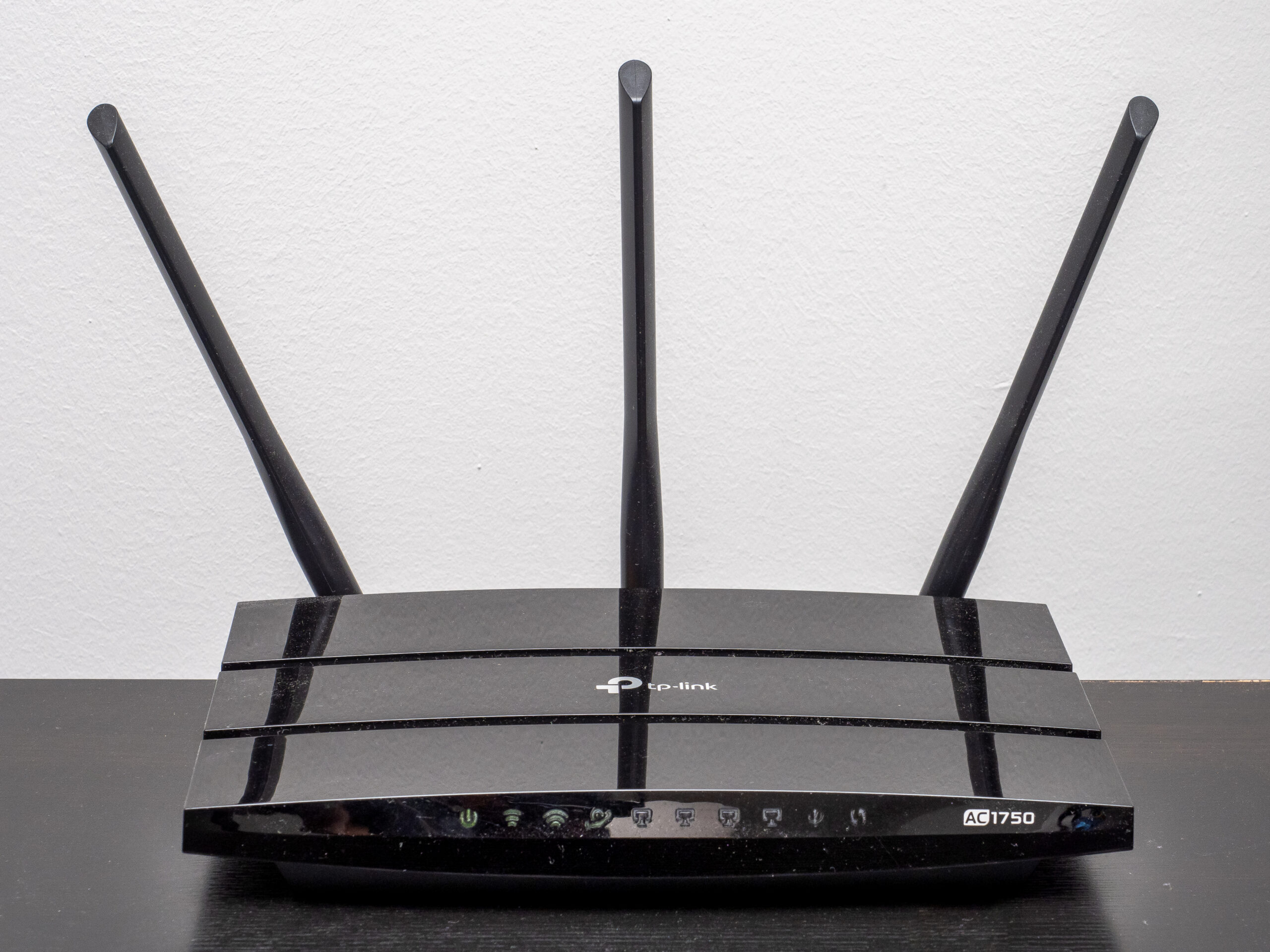A black wireless router with three upright antennas on a wooden surface